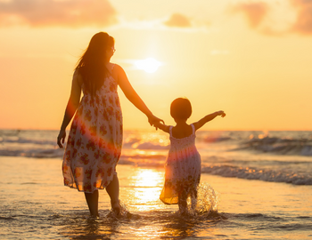 Mom and daughter on beach during sunset