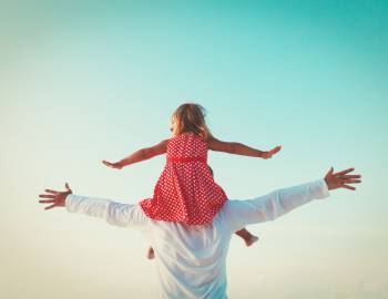 little girl on her dad's shoulders arms stretched out wide